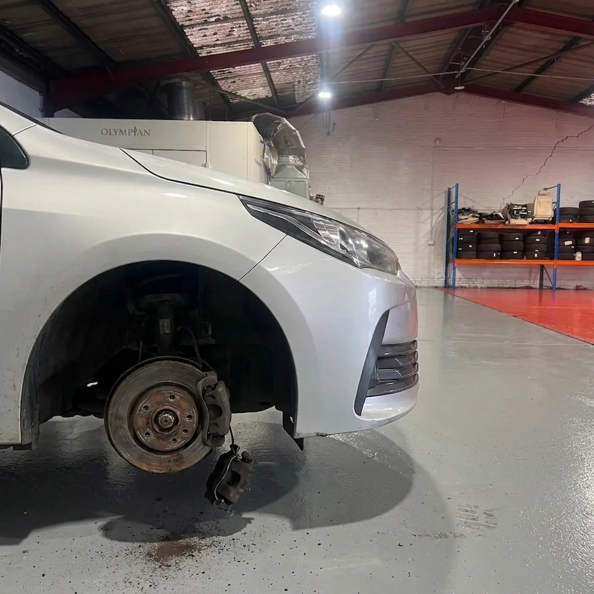 Silver saloon with the front wheel removed, showing a rusted brake disc and a caliper hanging loose beneath the hub.